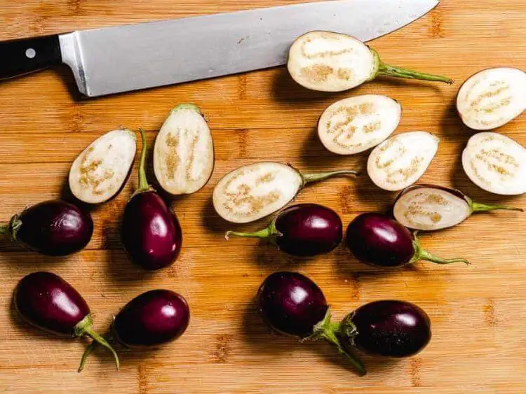 there are several whole baby eggplants alongside a few that have been sliced in half, arranged on a wooden cutting board.