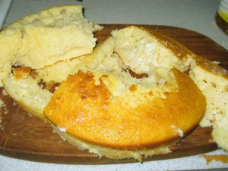 The image shows a cake that has fallen apart, lying in pieces on a wooden cutting board.