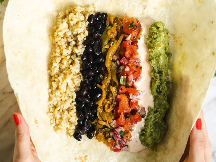 The image displays an open burrito held in someone's hands, showing its various fillings.