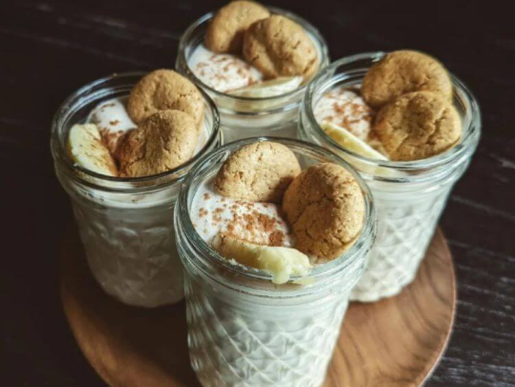 Three jars of banana pudding and cookies on a wooden table