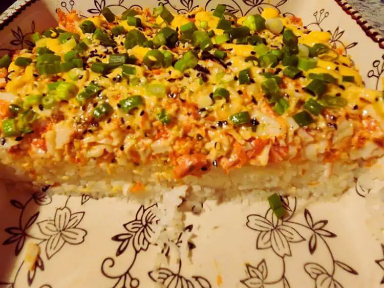 The image shows a casserole dish filled with rice, cheese, green onions, and sesame seeds.