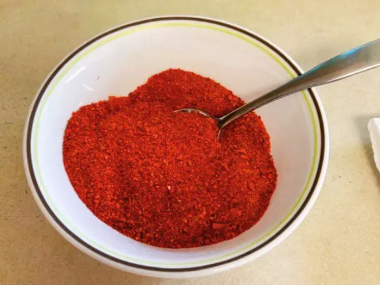 The image shows a white bowl filled with a bright red powder and a wooden spoon.