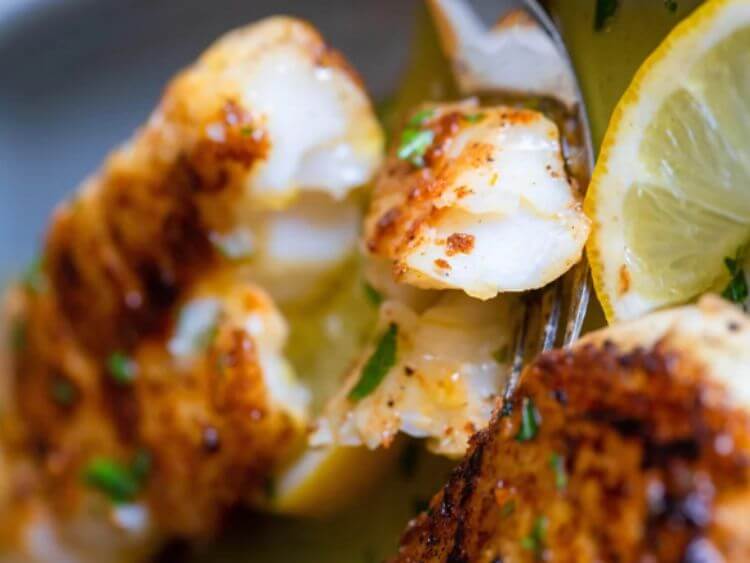 The image shows a close-up of a piece of salmon on a fork, glistening with a golden-pink hue