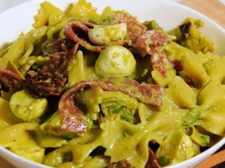 The image is of a bowl of pasta salad with avocado, mozzarella, and salami. It is a close-up of the salad, so we can see the individual ingredients in detail.