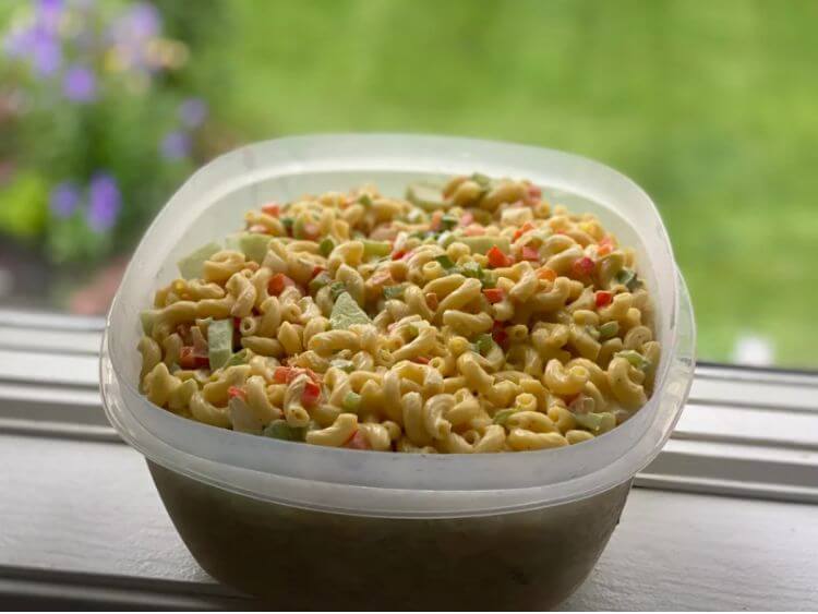 The image shows a bowl of macaroni salad sitting on a window.