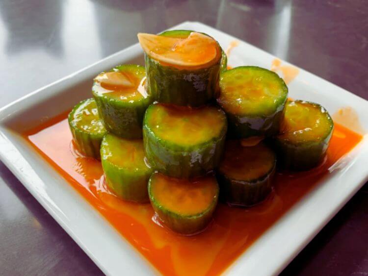 The image shows a plate of sliced cucumbers, cut into thick rounds and stacked neatly.