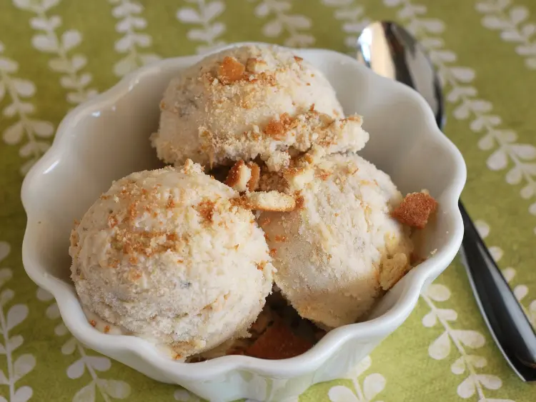 three scoops of ice cream presented in a white bowl, which is placed on a green surface with a floral pattern.