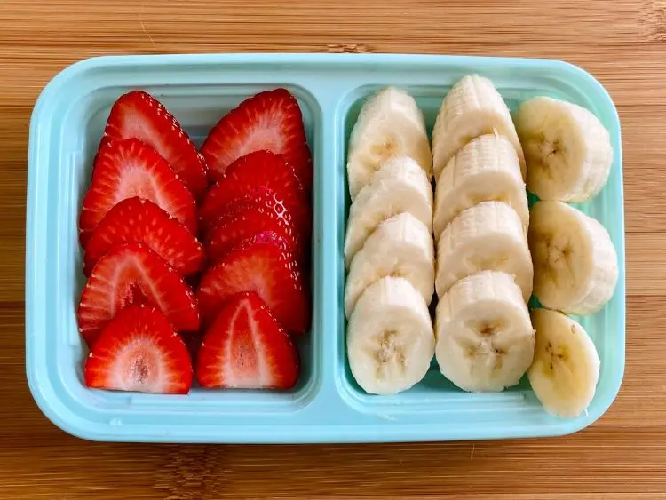 The image shows a light blue plastic container with two sections, each filled with sliced fruit.