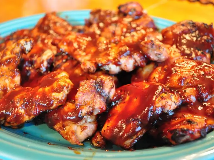 A platter of barbecued ribs and chicken pieces generously coated with a glossy barbecue sauce.