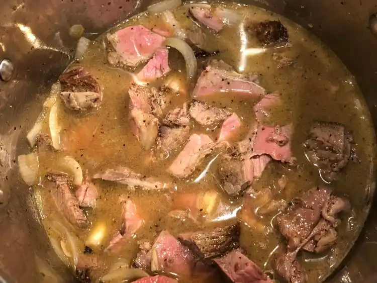 a pot containing what appears to be a stew or broth with chunks of cooked meat, some pieces exhibiting a pinkish hue indicative of medium doneness.